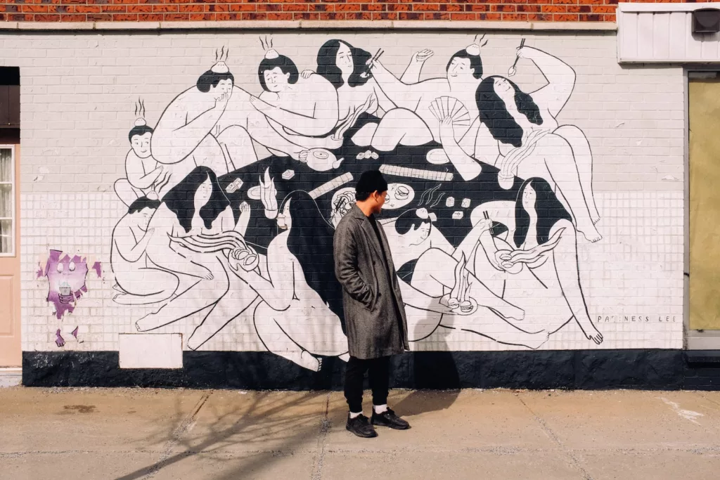 Person in a grey coat standing in front of wall with graffiti, an independent art business